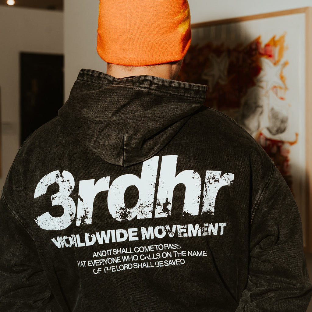 Person wearing a black hoodie with '3rdhr Worldwide Movement' text and an orange beanie indoors.